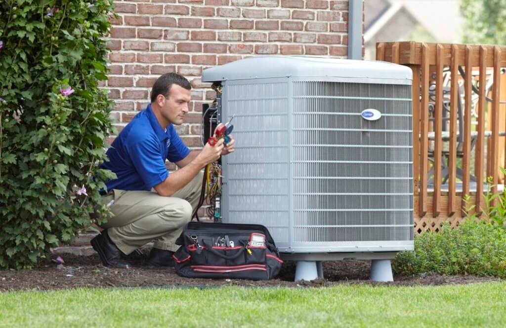 Technician kneeling next to an outdoor AC unit with tools.
