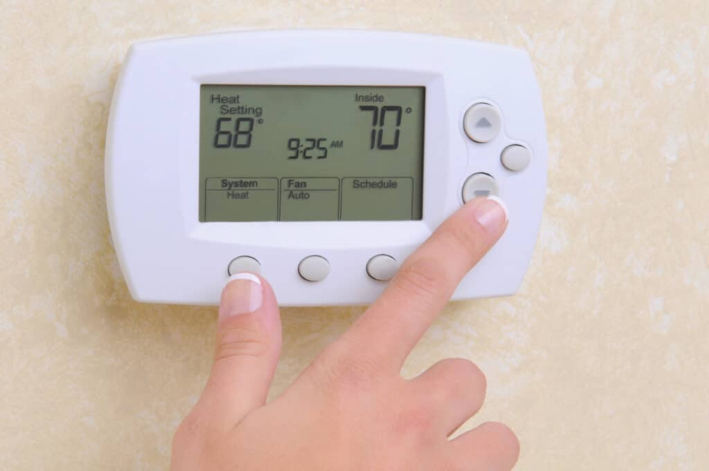 A white thermostat on a beige wall and a hand lowering the temperature